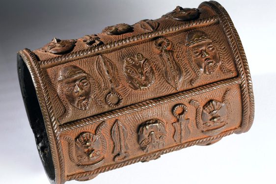 Brown-orange bronze armlet, shaped like a tube, decorated with bold symbols in relief.